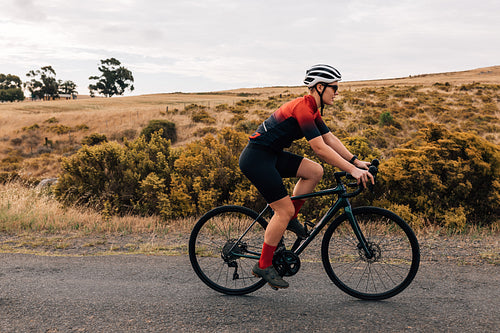 Side view of fit and determined sportswoman cycling road bike on a countryside road