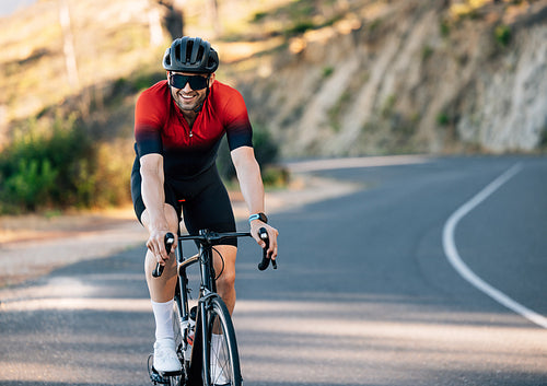 Smiling cyclist on a road bike going down a countryside road. Cheerful cyclist in sports attire.