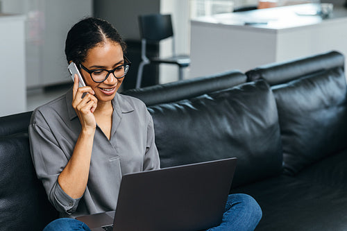 Beautiful woman using a smartphone having phone call from her apartment. Businesswoman enjoying conversation sitting on a couch.