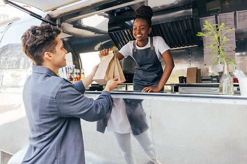 Side view of a young man taking packages with street food from a saleswoman