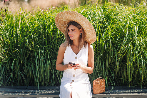 Stylish blond woman holding a smartphone while sitting in the park