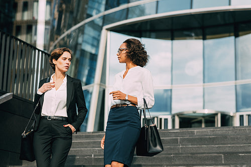 Young businesswoman discussing with her colleague while walking down the stairs near an office building