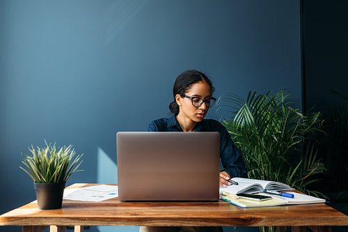 Thoughtful young woman looking at documents in home office. Entrepreneur working remotely.