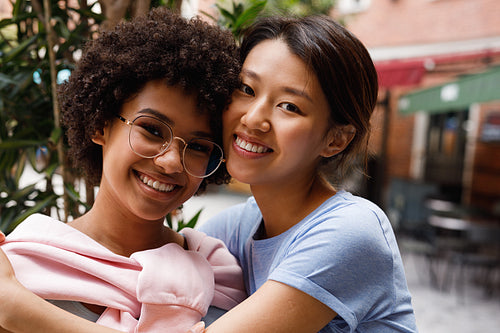 Two smiling friends looking at a camera, standing outdoors