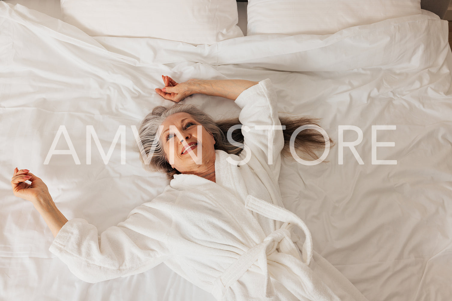 Senior woman in a bathrobe looking up while lying on a bed. Smiling retired female enjoying morning.