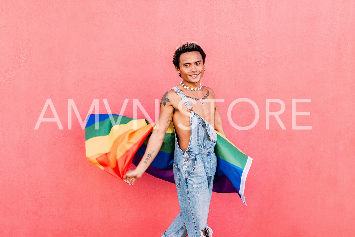 Smiling young gay man standing with pride flag. Happy guy in casuals holding LGBT flag outdoors.