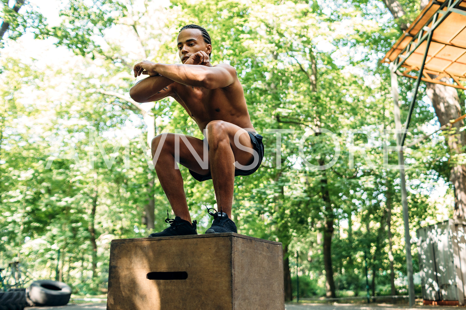 Athlete doing box jumping on sports ground. Young male performing squats on wooden box.