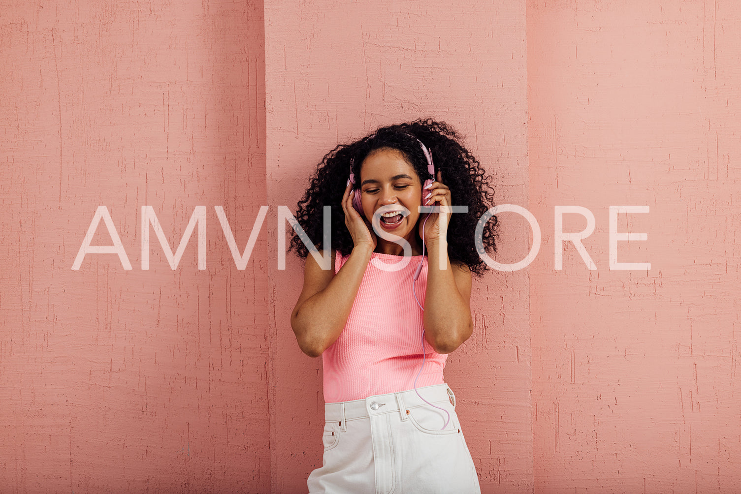 Happy woman with curly hair holding pink headphones with closed 