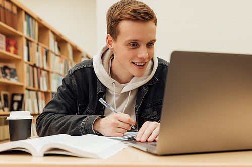 Smiling guy looking at laptop screen while sitting in library