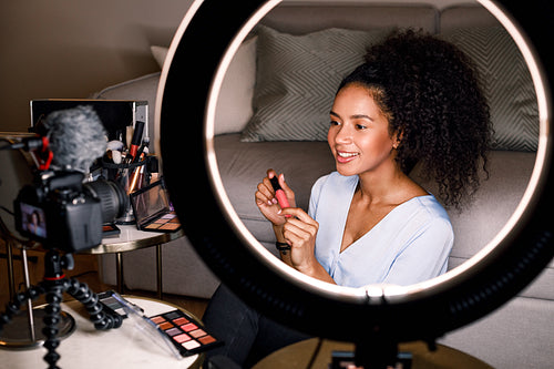 Smiling beauty vlogger recording video for her channel using ring light and digital camera