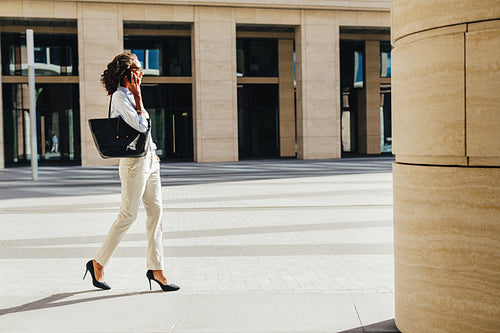 Woman carrying handbag on shoulder walking on city street from office