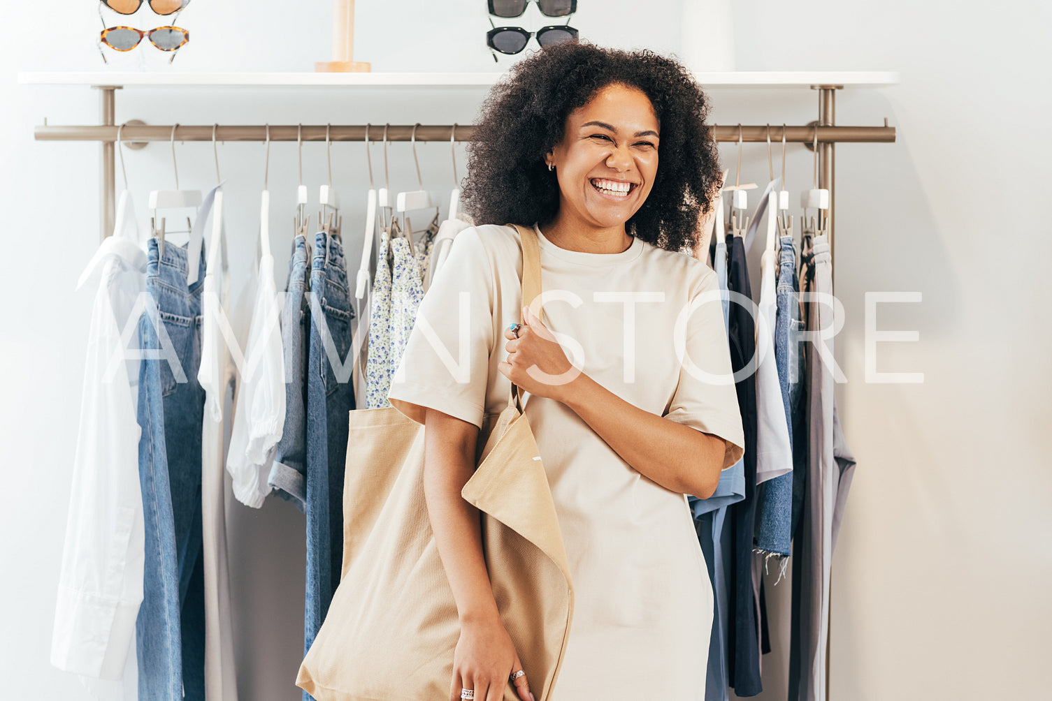 Laughing woman with shopping bag standing in clothing store at rack