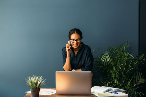 Young businesswoman standing leaning to a chair in living room while talking on cell phone