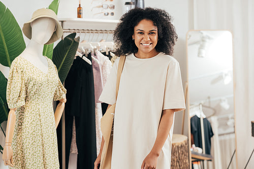 Portrait of a woman in stylish clothes and shopping bag standing in a small boutique