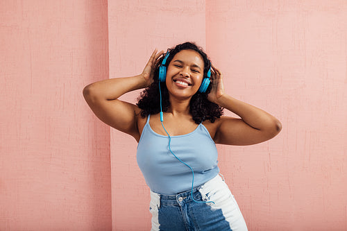 Happy woman with curly hair enjoying music listening by blue headphones