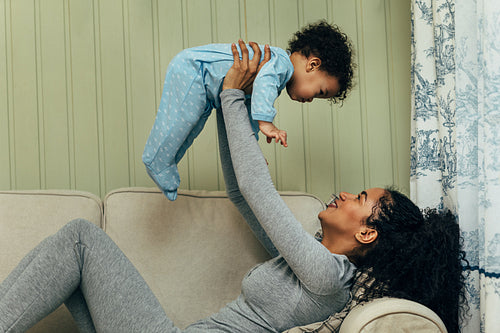 Young mother sitting on a sofa and lifting her baby in living room