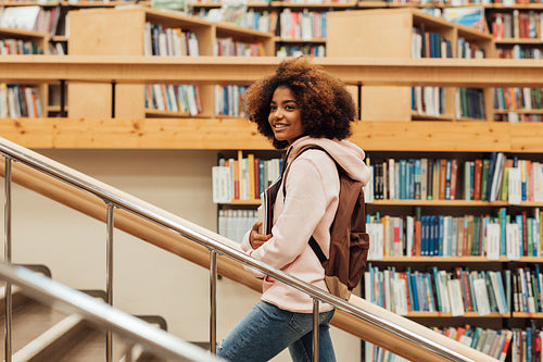 Smiling girl walking on stairs in library. Student in college library.