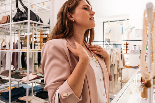 Side view of stylish woman try on a necklace in a small fashion