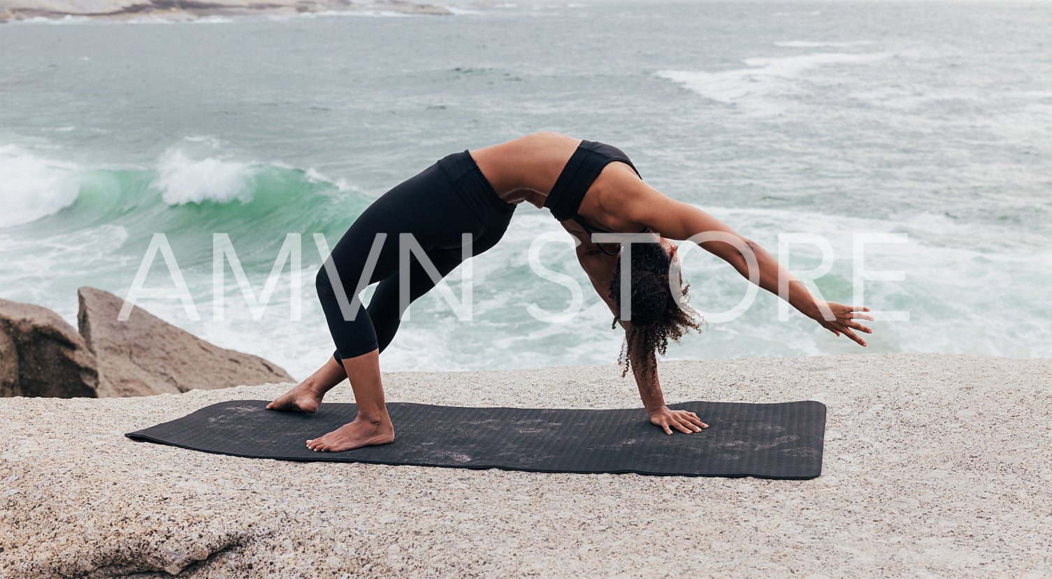 Side view of slim woman practicing yoga on a mat by ocean