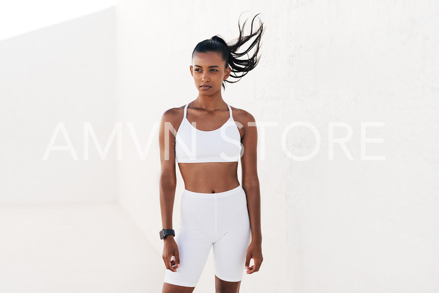 Young slim woman in white sportswear relaxing outdoors. Sportswoman taking a break at white wall outdoors.