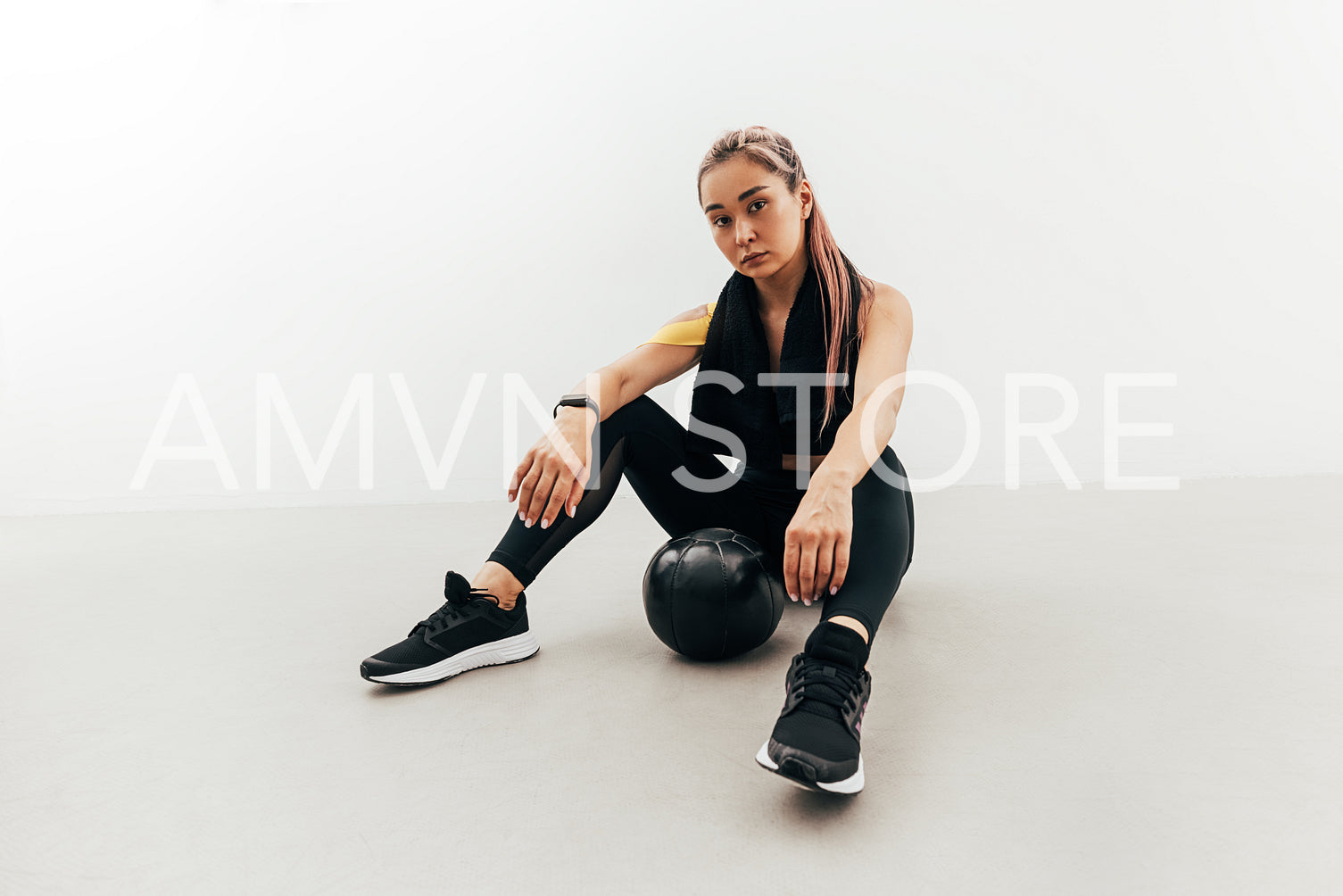 Woman in sports clothes and with black towel on her neck relaxing after exercises with a medicine ball