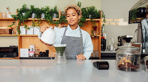 Woman barista pouring water from kettle to a filter at counter