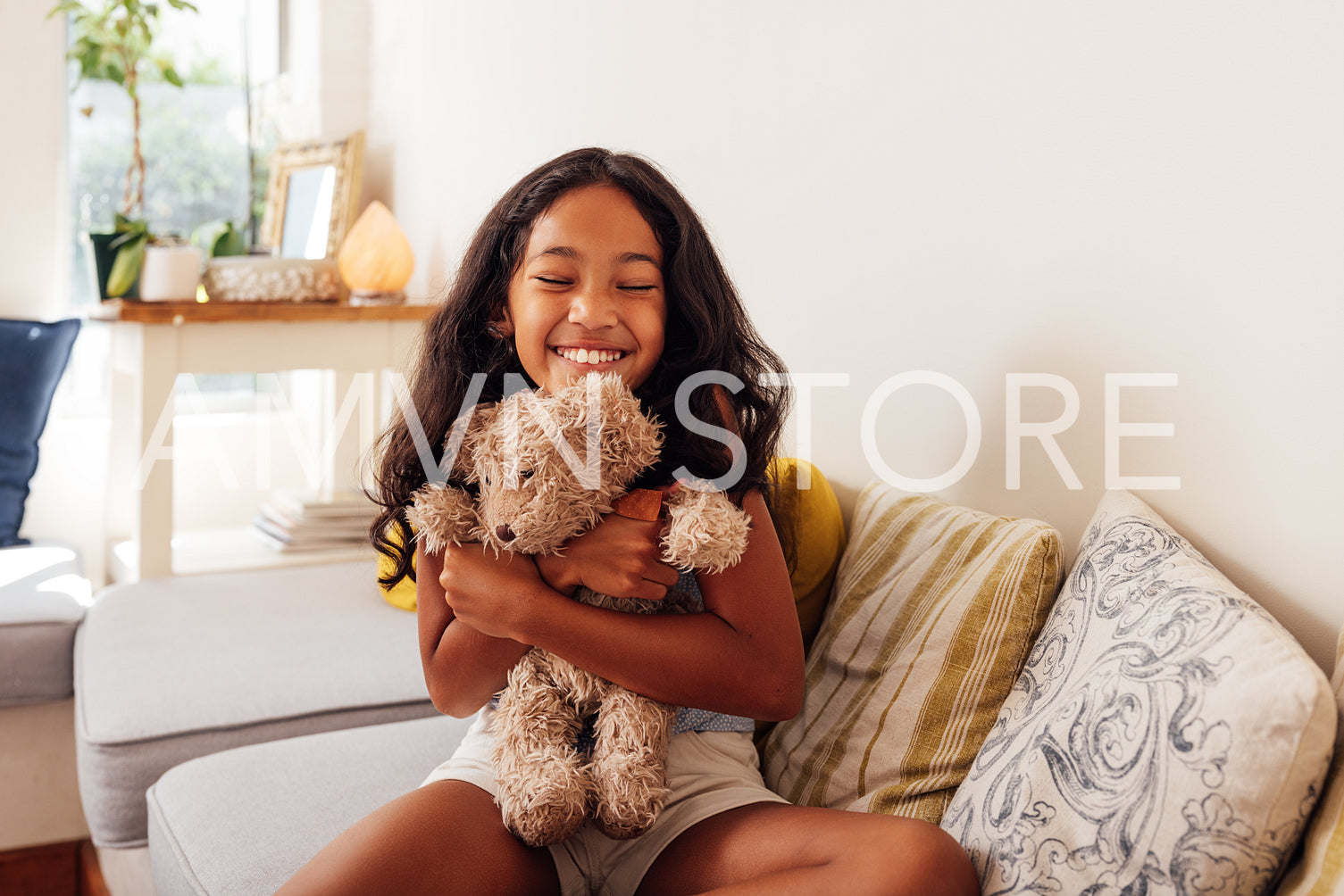 Happy girl with closed eyes hugging her favorite toy while sitting on a sofa in the living room