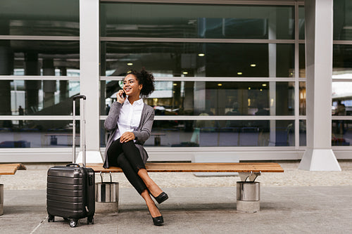 Young businesswoman sitting on a bench and talking on smartphone at airport terminal