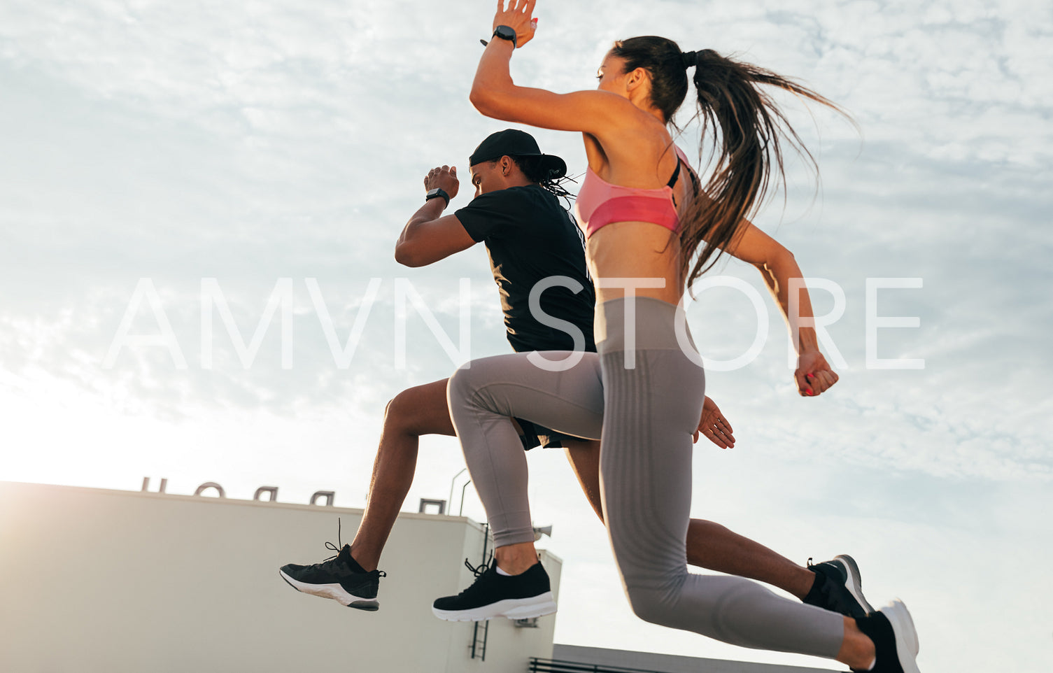 Two athletes jumping in the air during run. Man and woman sprinting together on the roof.