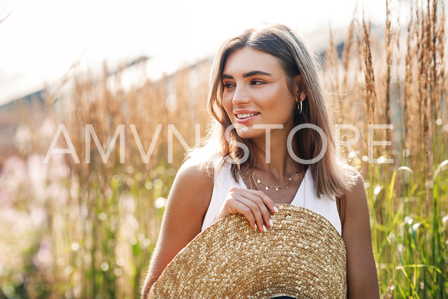 Smiling woman standing outdoors with big straw hat surrounded by tall grass	