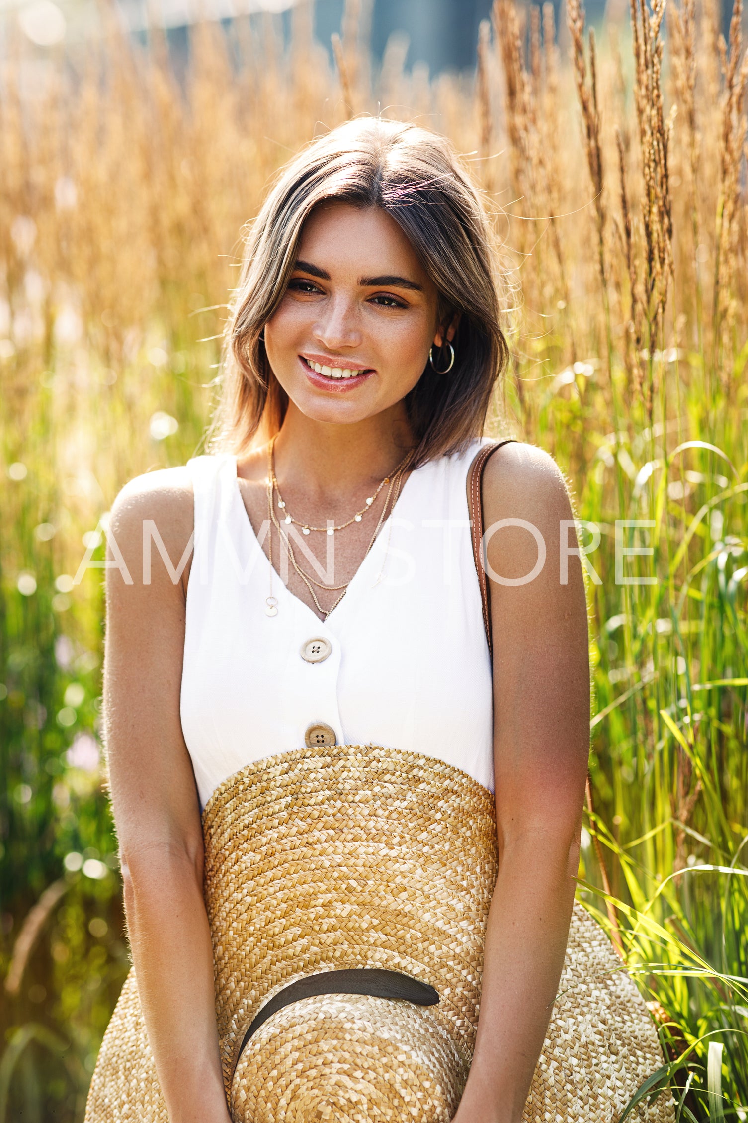 Stylish woman standing on a field and holding a straw hat	