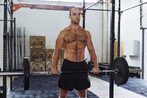 Fit male athlete exercising with heavy weights at training gym.