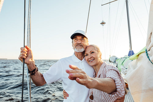 Happy mature woman pointing into the distance while embracing by his husband on their yacht