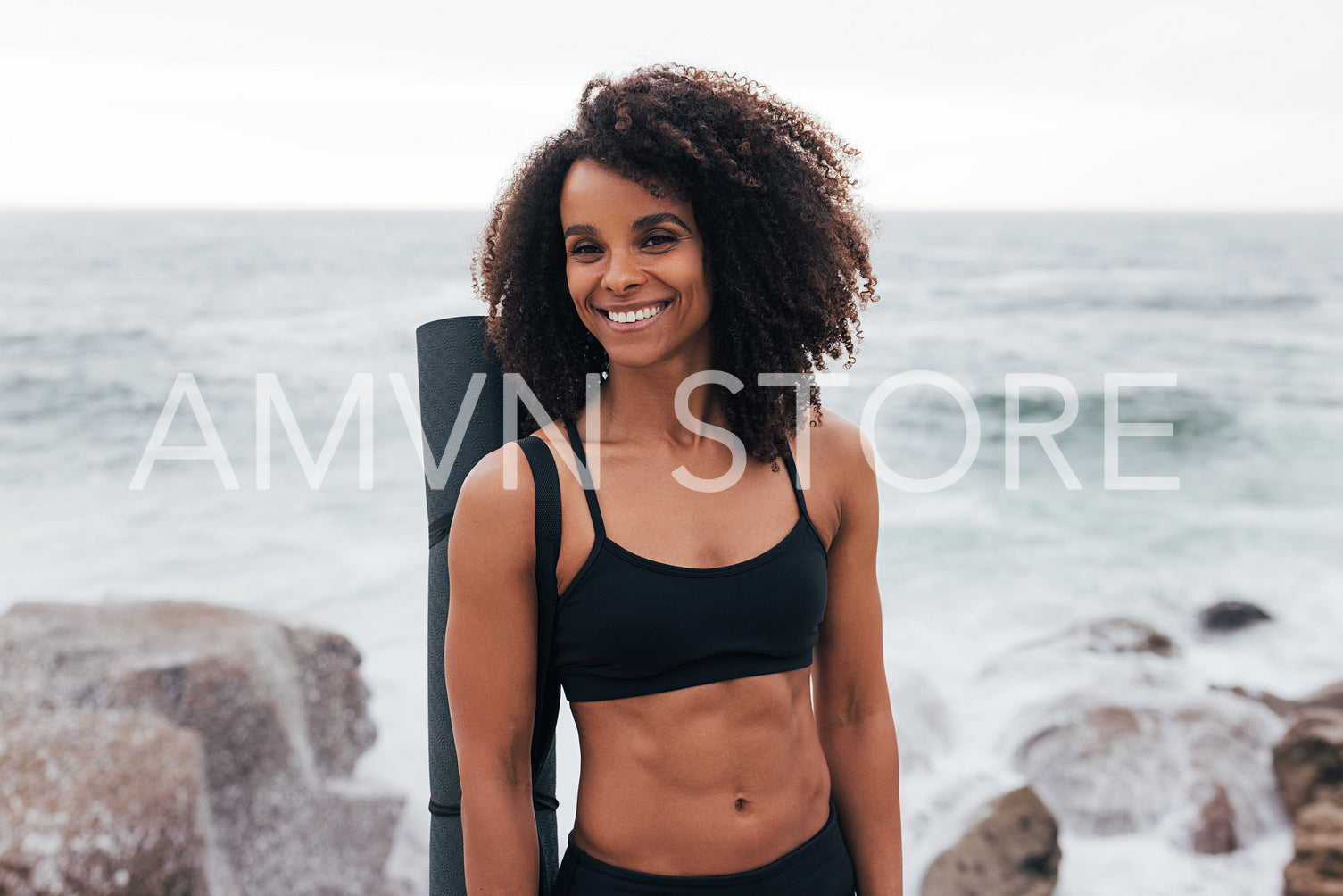 Portrait of a muscular woman with a mat standing by the ocean and looking away