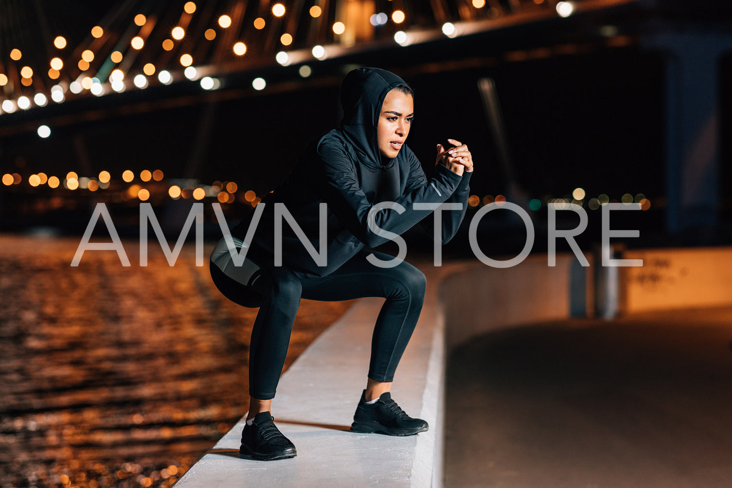 Woman in hooded sport shirt doing squats on embankment at night