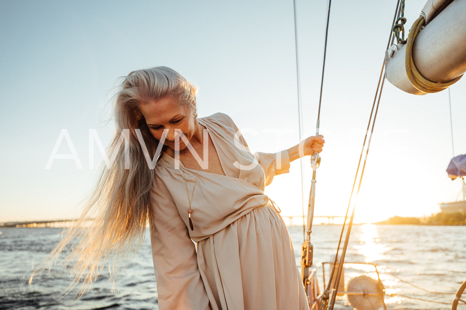 Beautiful mature woman with long gray hair standing on a sailboat and looking down at sunset	