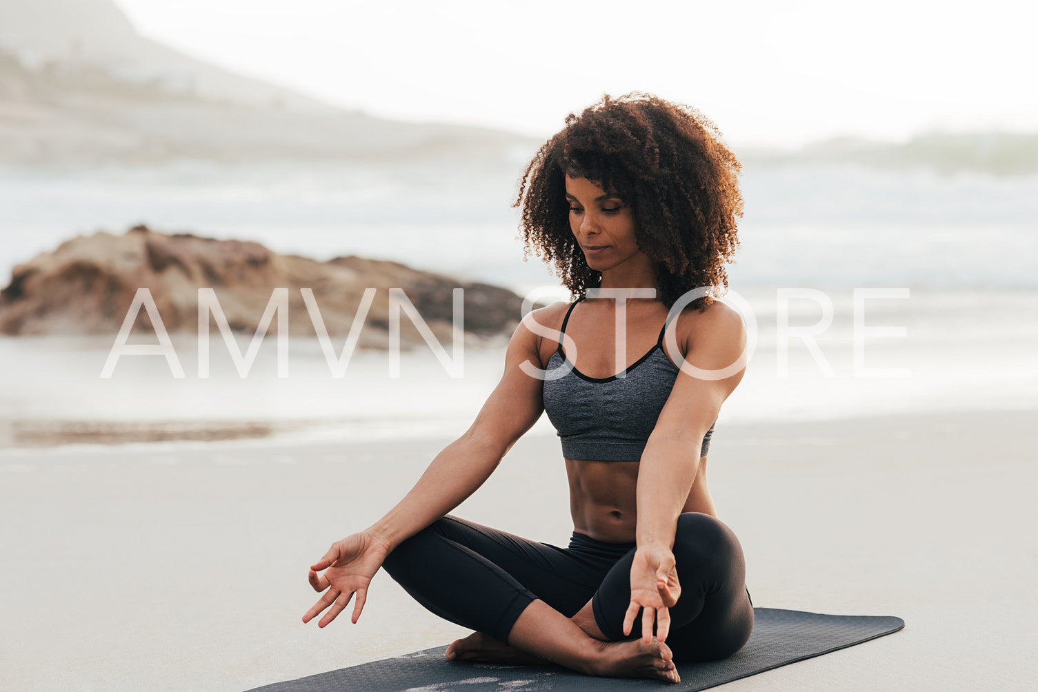 Woman with closed eyes doing yoga asana meditation on the beach. Female in sport clothes sitting in lotus pose on mat at sunset.