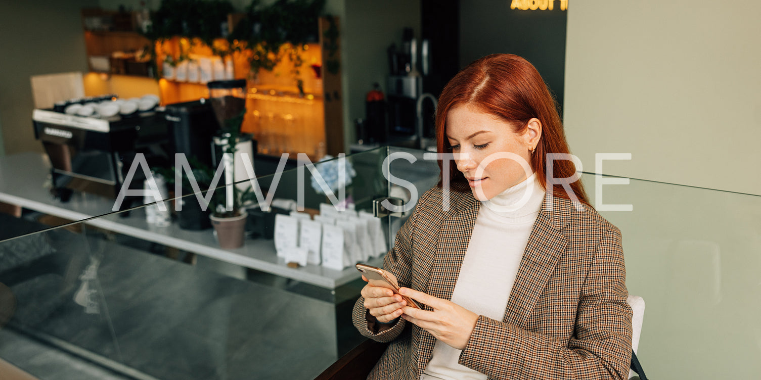 Beautiful female with ginger hair holding a mobile phone. Businesswoman in formal wear typing on a mobile phone.