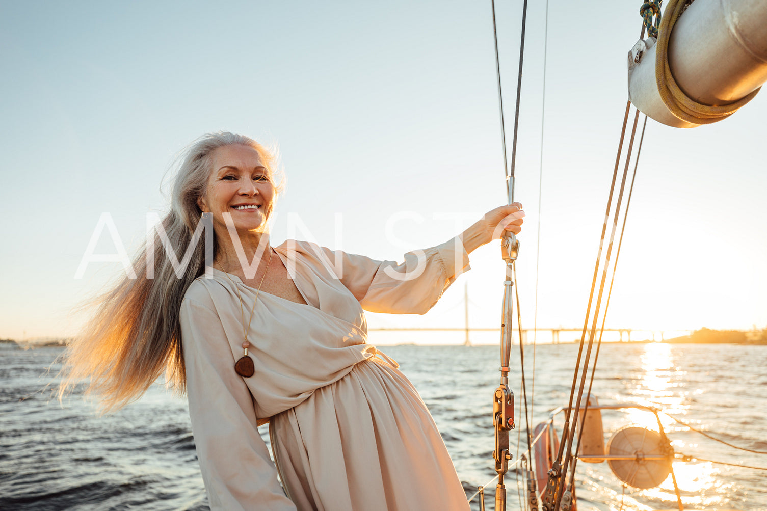 Smiling female wearing dress on private yacht. Senior woman with long white hair looking at camera.	