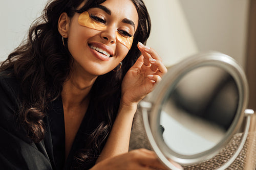 Close up of beautiful brunette looking at mirror while applying eye patch