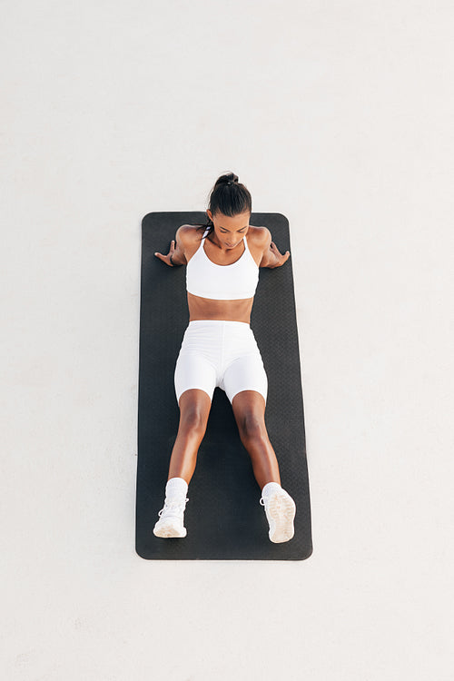 Shot from above of a young sportswoman relaxing on a mat. Female in white fitness wear taking a break.