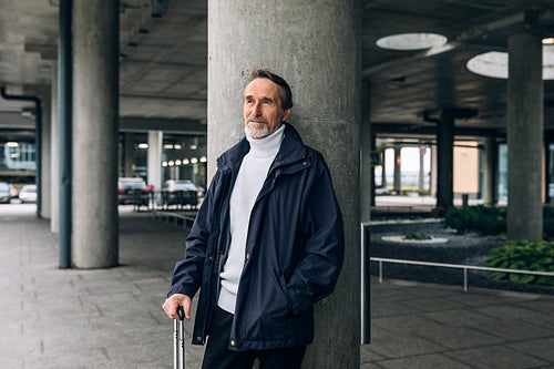 Stylish senior man standing outdoors at airport terminal looking away