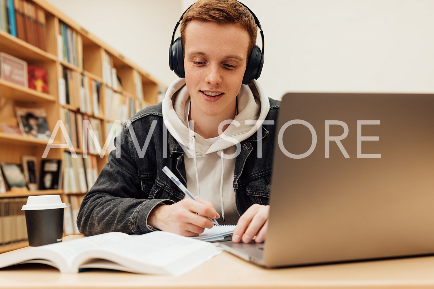 Smiling guy in headphones sitting at desk in library and writing