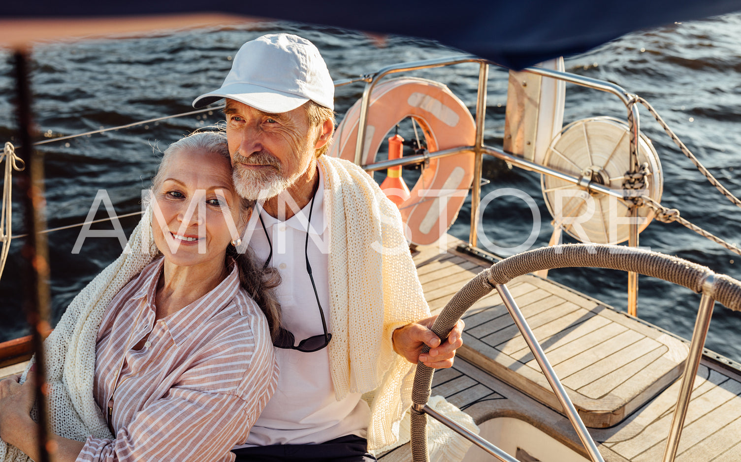 Mature couple sitting on yacht and wrapped in blanket. Elderly people enjoying a vacation on sailboat.	