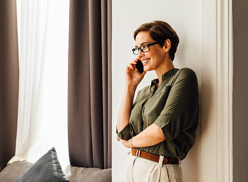 Caucasian businesswoman leaning a wall in apartment talking on mobile phone