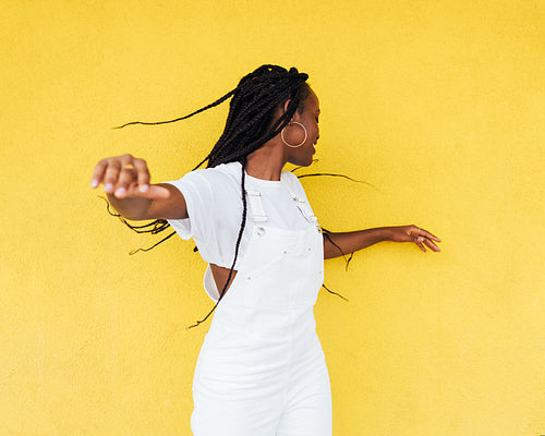 Young woman in white overall having fun against a yellow wall outdoors