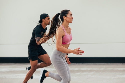 Two athletes running together outdoors. Woman and man sprinting on the rooftop.