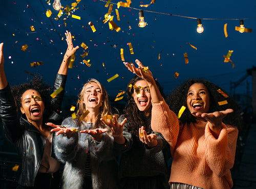 Outdoor shot of group friends laughing under confetti