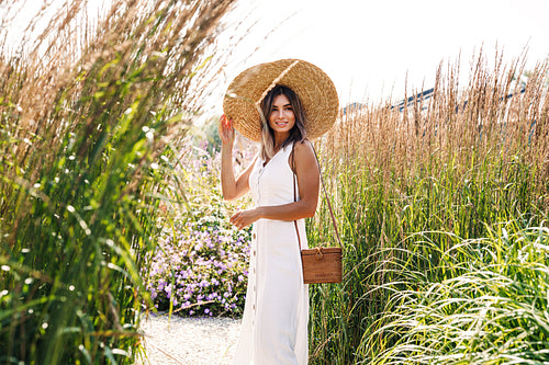 Young stylish woman in a big straw hat standing on the field