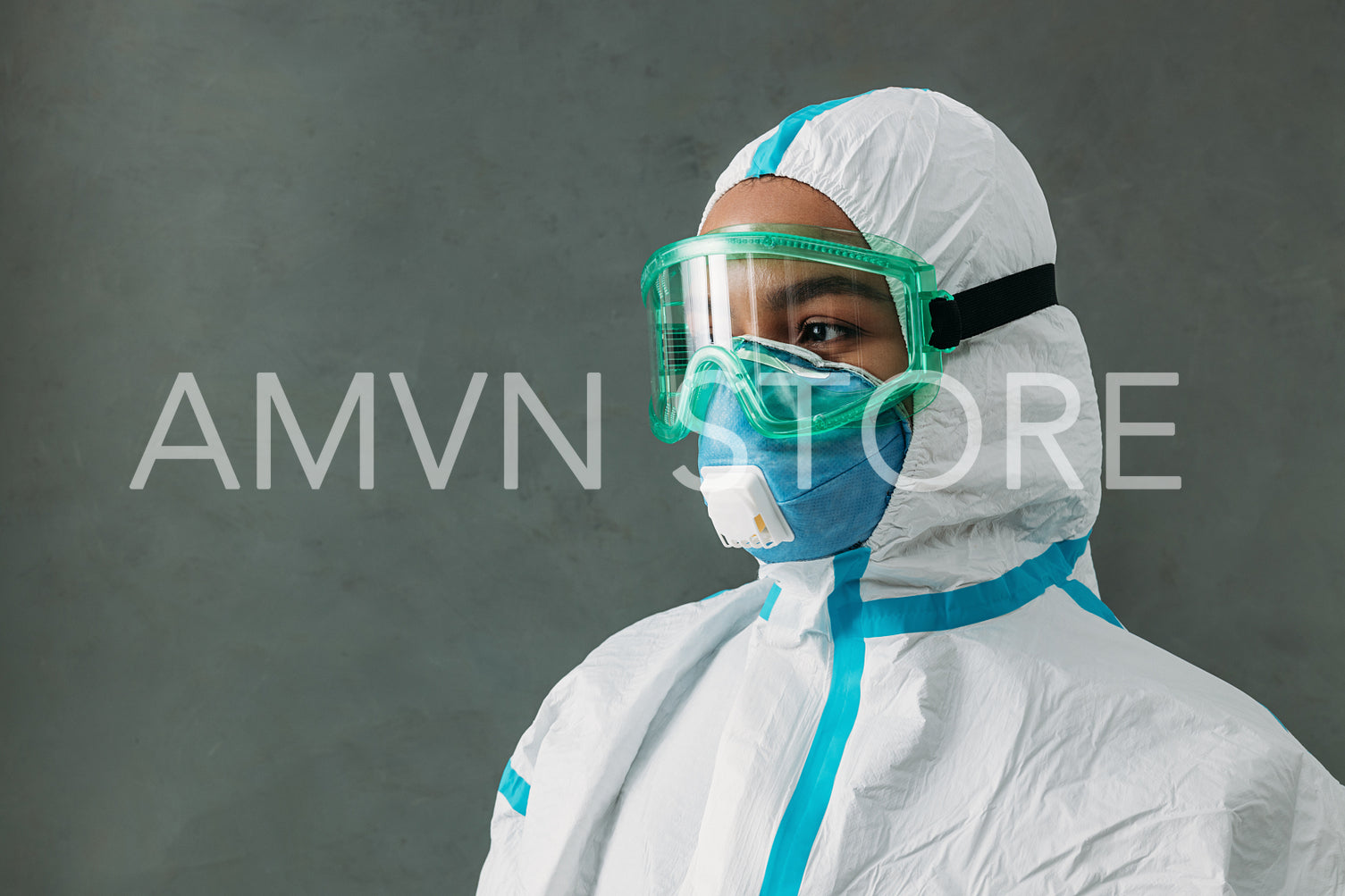 Close up of medical specialist in a protective suit with a respirator and glasses standing at wall looking away	